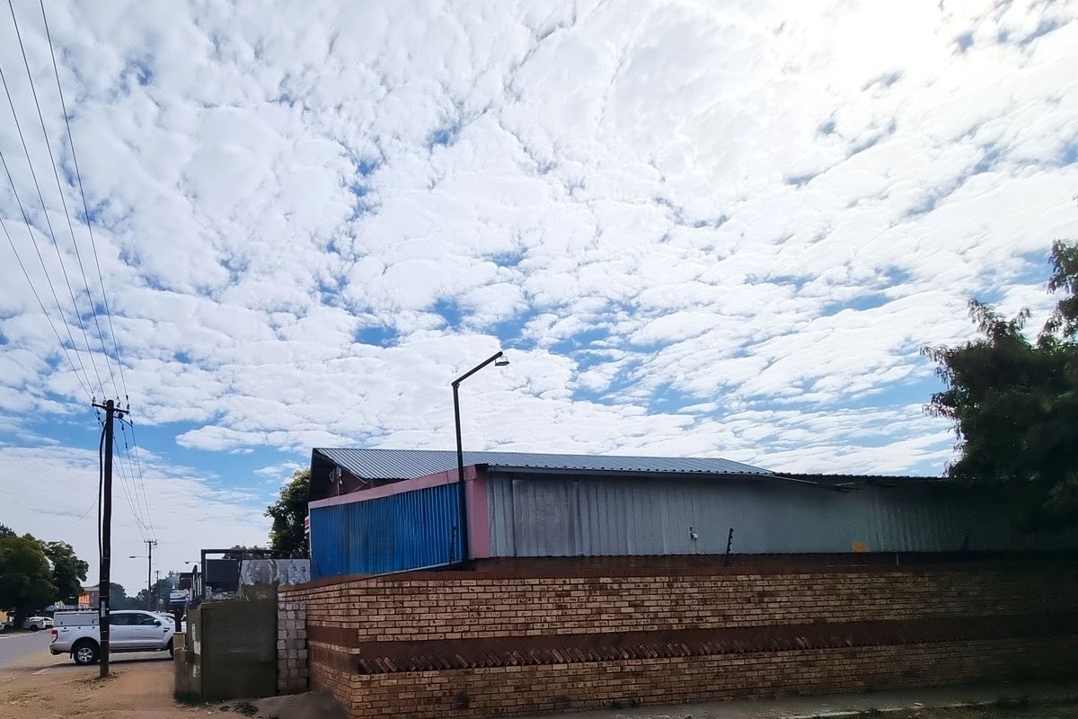 Exterior view of a commercial property featuring a corrugated metal roof, brick boundary wall with security spikes, and metal cladding.