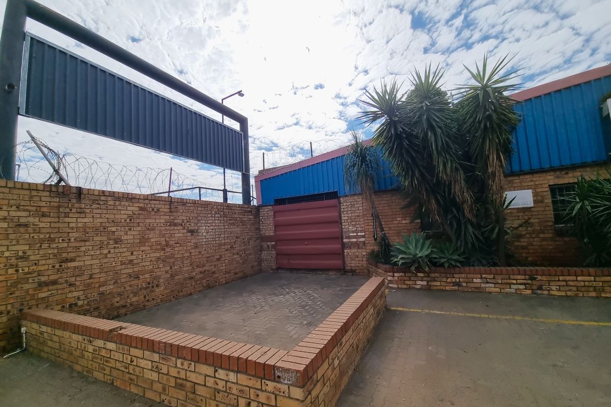 Rear exterior courtyard area featuring face brick walls, a metal roller shutter door, and secure perimeter fencing with razor wire.