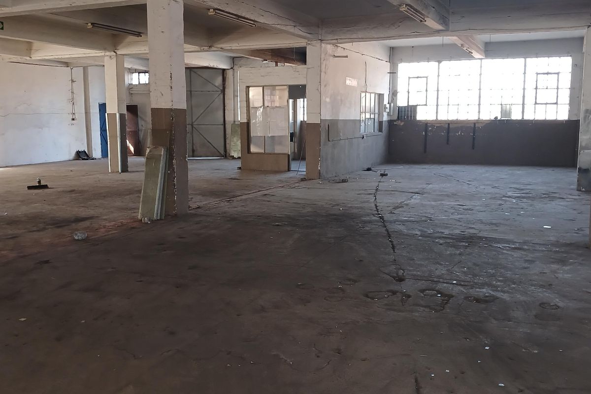 Expansive industrial warehouse space featuring high ceilings, concrete flooring, and large windows providing natural light, suitable for various commercial or storage applications.