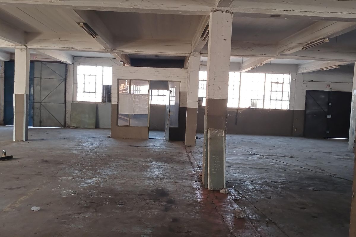 Spacious industrial warehouse featuring high concrete ceilings, exposed structural columns, large steel-framed windows, and durable concrete flooring throughout the open-plan facility.