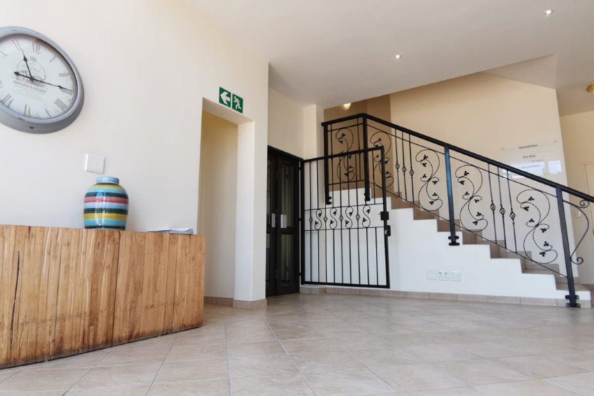 A bright office building lobby featuring tiled flooring, a decorative wrought iron staircase railing, and a secure gated access point.