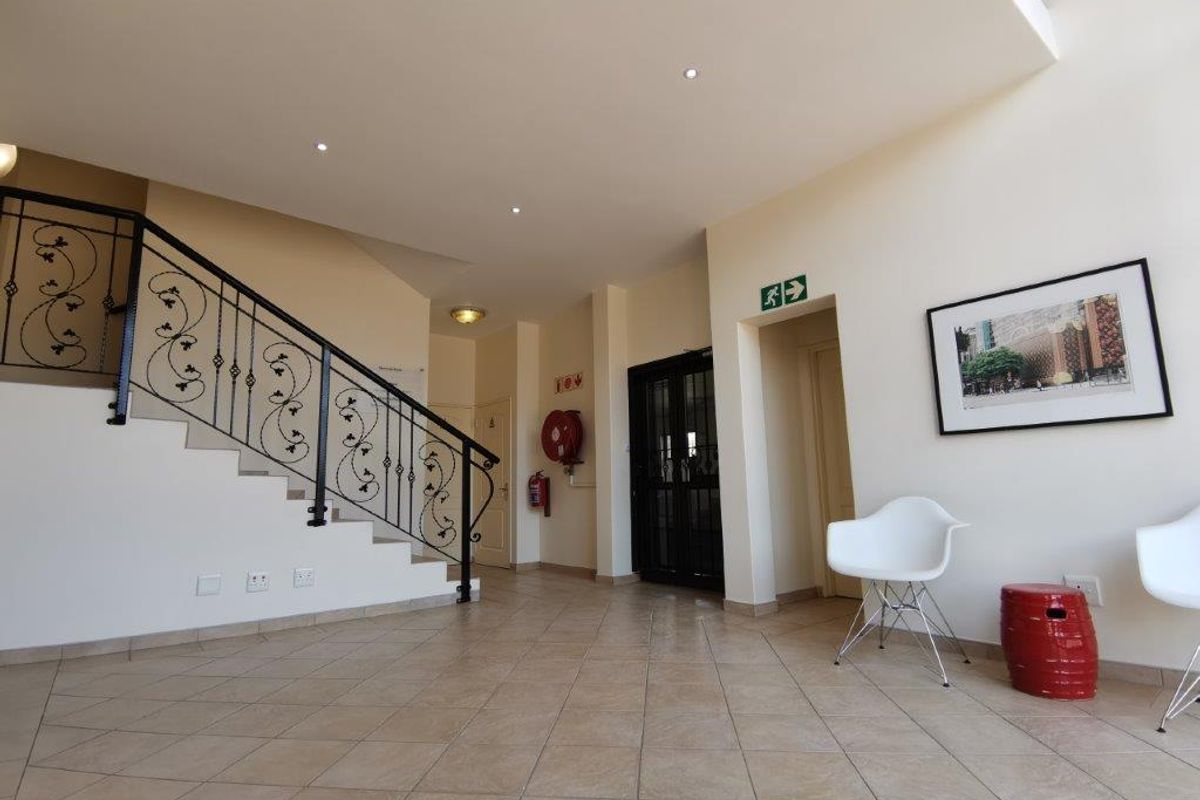 Spacious office building entrance foyer featuring tiled flooring, a decorative wrought iron staircase railing, and integrated recessed ceiling lighting.