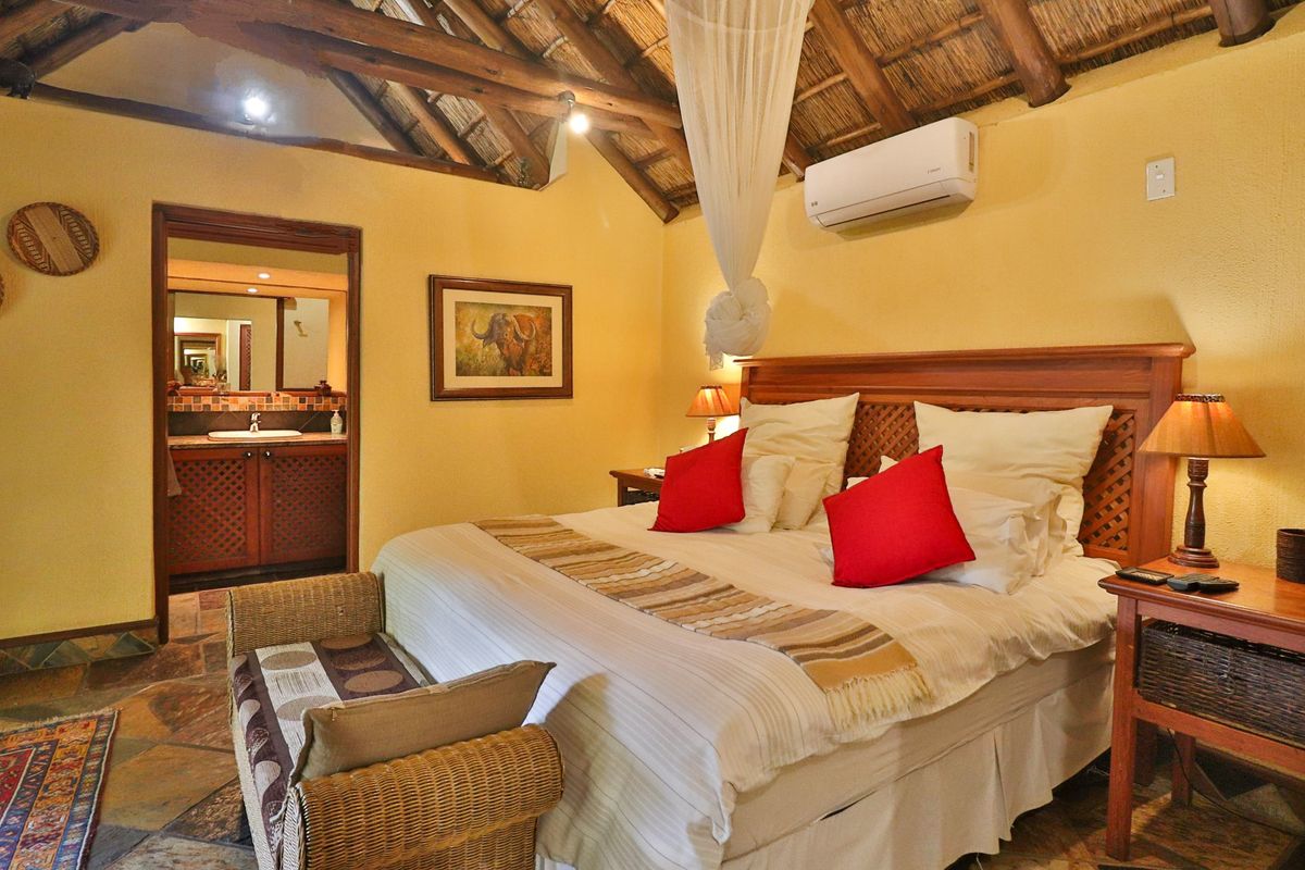 A cozy bedroom featuring a traditional thatched roof with exposed timber rafters, stone flooring, and an adjoining en-suite bathroom.