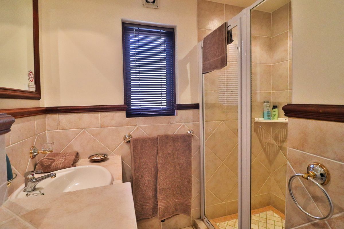 A functional bathroom featuring a shower enclosure, vanity basin, and neutral wall and floor tiling with classic wooden trim accents.