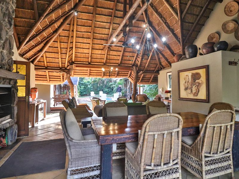 Spacious open-plan living and dining area featuring a high thatched roof with exposed timber trusses, a stone fireplace, and direct access to the patio.