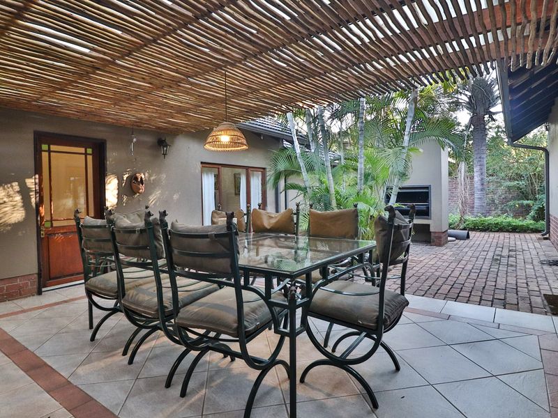 A covered outdoor patio featuring a timber slat pergola, built-in braai, and tiled flooring, ideal for alfresco dining and entertaining.