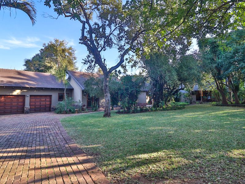 Front view of the guest house featuring a double garage, brick paved driveway, and a well-maintained garden with mature trees.