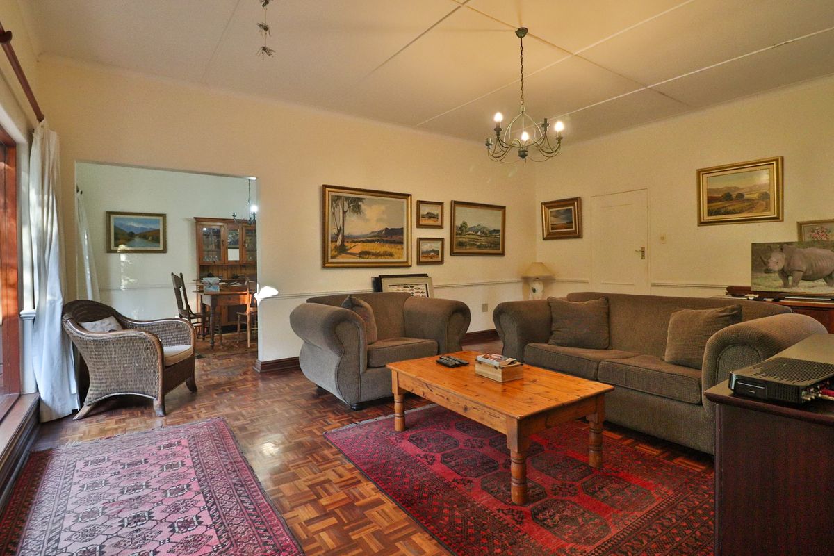 A traditional living room featuring classic parquet flooring, a central chandelier, and a dado rail, with an adjacent dining area visible through the opening.