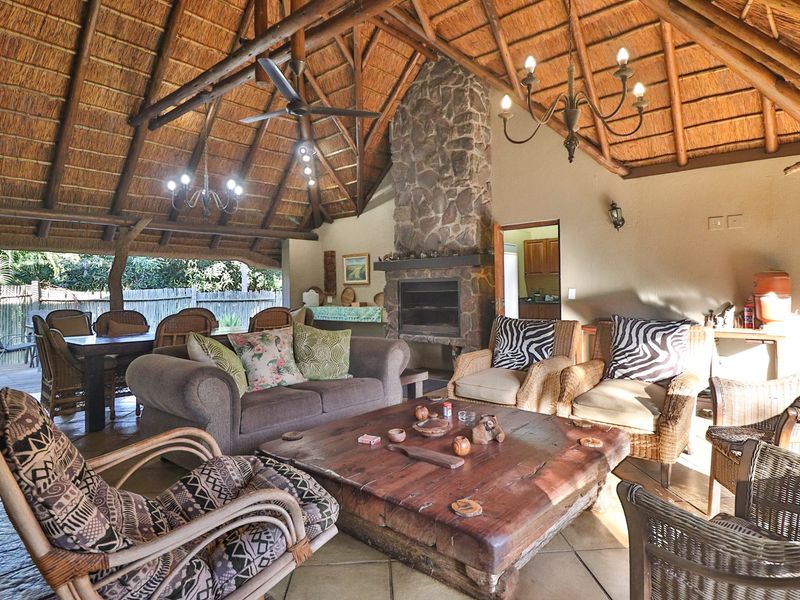 Spacious covered patio featuring a high thatched roof with exposed timber trusses, a stone fireplace, and tiled flooring, ideal for outdoor entertaining.