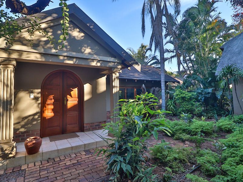 A charming guest house entrance featuring arched wooden double doors, classical columns, and a well-maintained garden with brick paving.