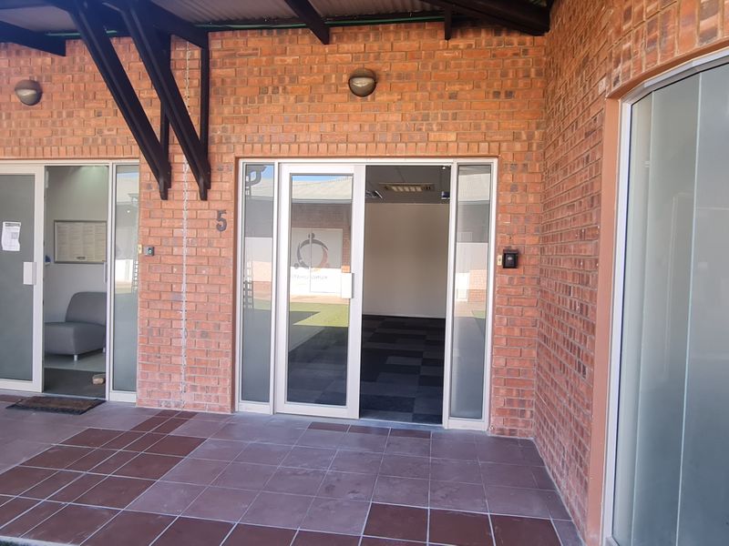 A covered patio area featuring exposed brickwork, tiled flooring, and glass sliding door access to office units.