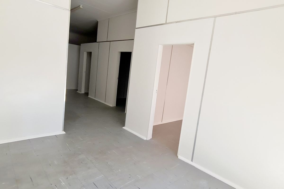 An empty retail interior featuring modular wall partitioning, grey tiled flooring, and multiple access points to secondary spaces.
