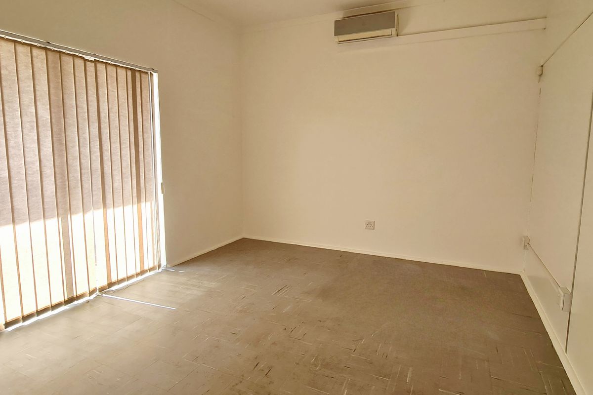 A vacant office or retail space featuring neutral walls, vertical blinds, and a wall-mounted air conditioning unit.