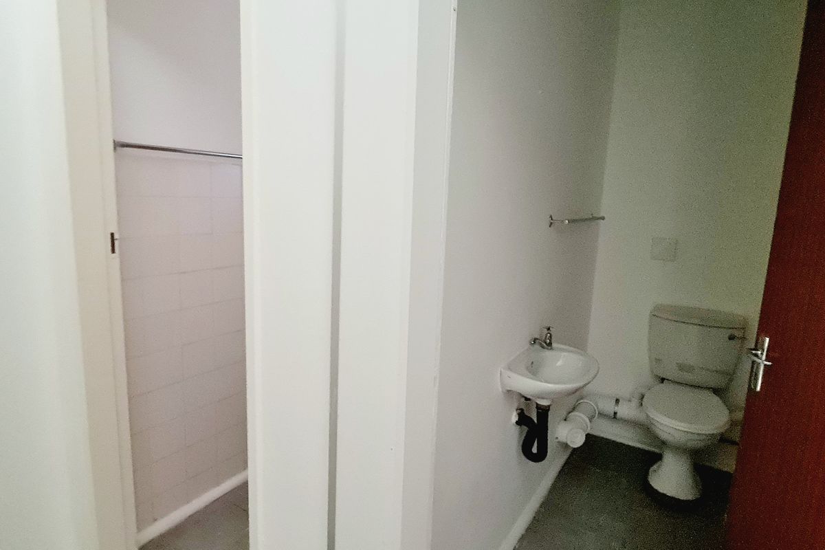 A functional bathroom featuring a toilet, wall-mounted basin, and a separate shower area with tiled walls.