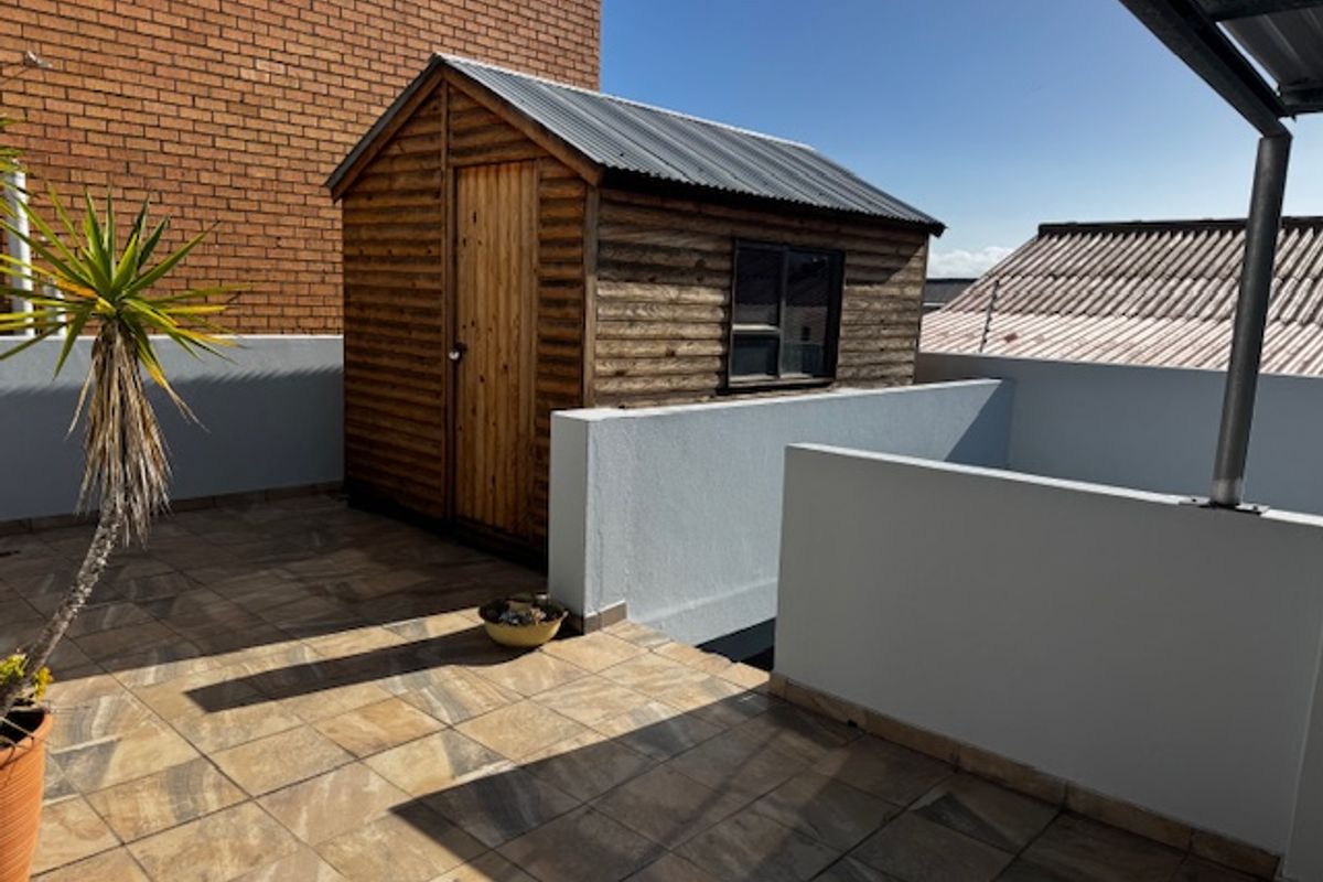 A tiled outdoor balcony area featuring a timber storage shed with a corrugated metal roof and surrounding parapet walls.