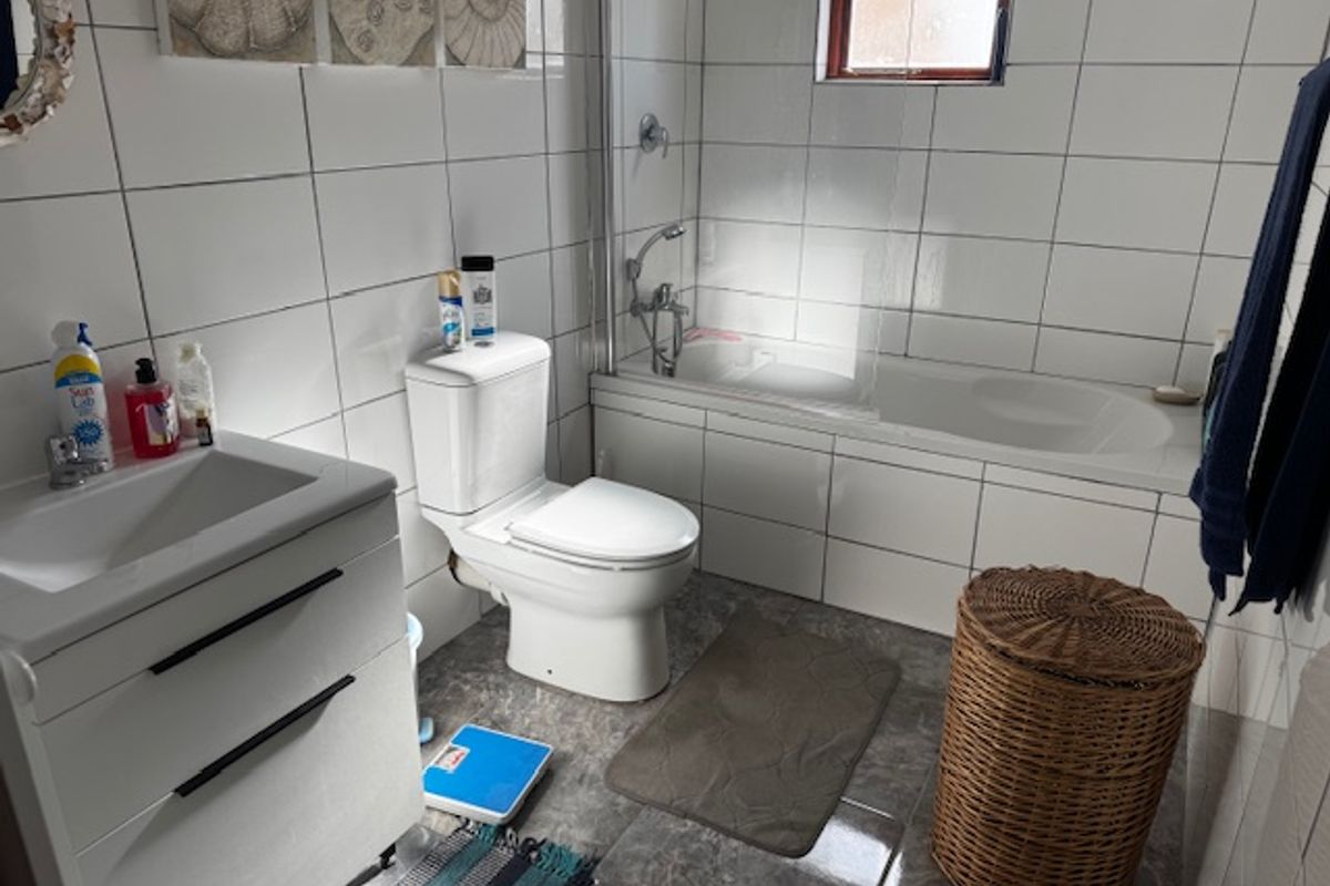 A functional bathroom featuring a white vanity, toilet, and a bathtub with a glass shower screen, finished with neutral wall and floor tiling.