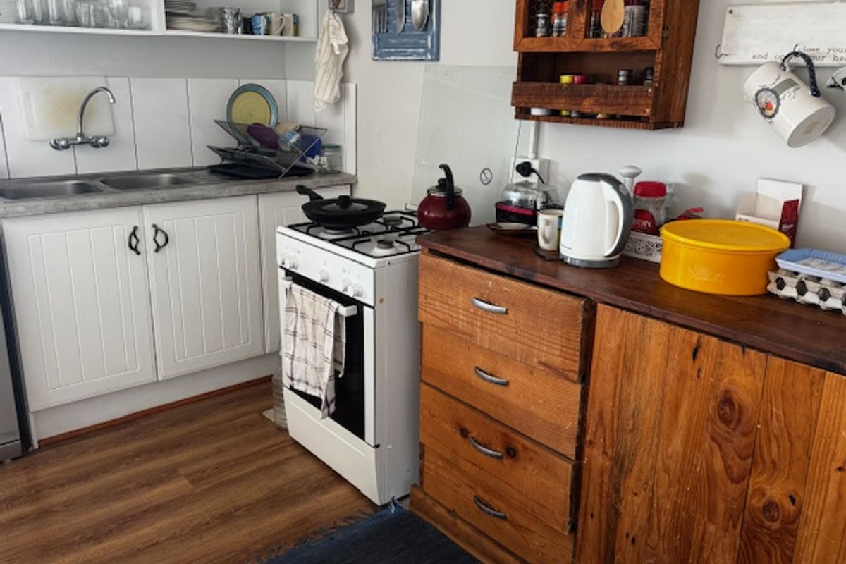 A functional kitchen area featuring a gas stove, double sink, tiled backsplash, and a mix of white and natural wood cabinetry.