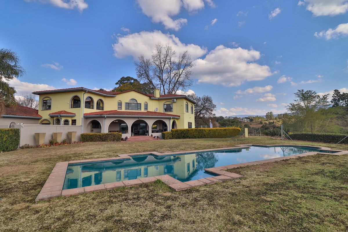 Rear view of a large farm-style residence featuring a swimming pool, expansive lawn, and a covered patio with arched architectural details.