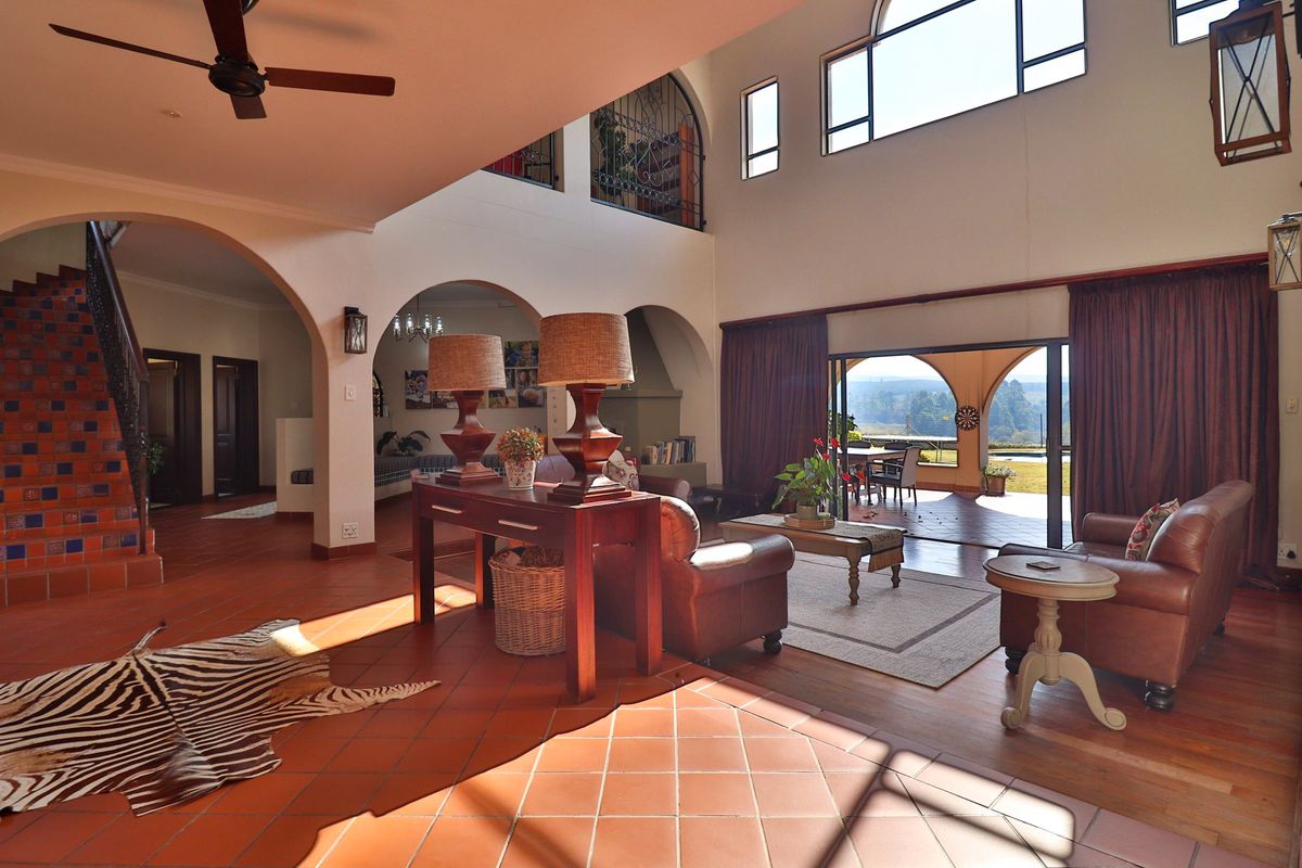 Spacious double-volume living area featuring terracotta flooring, arched architectural details, a mezzanine level, and large sliding doors opening to a scenic outdoor patio.