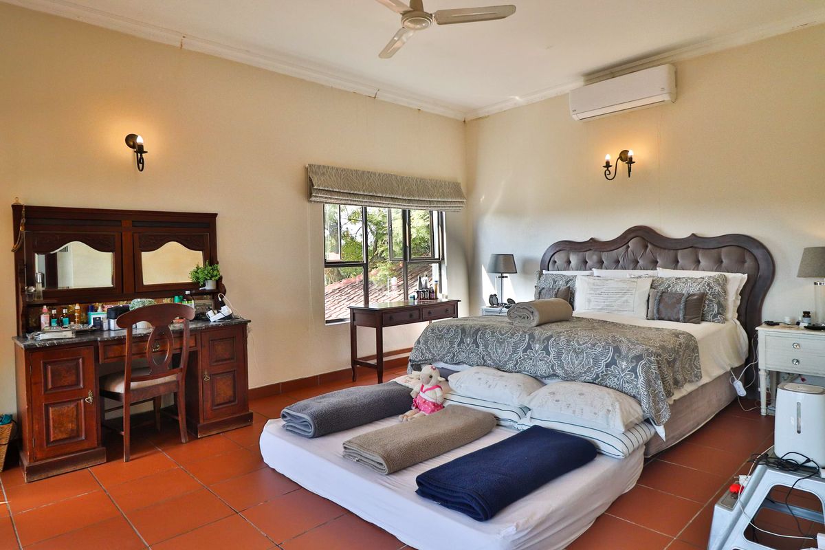 Spacious bedroom featuring terracotta tile flooring, a ceiling fan, and a wall-mounted air conditioning unit, offering a comfortable and functional living space.