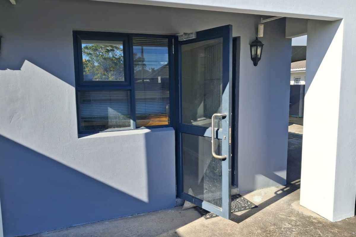 A modern office entrance featuring a grey exterior facade, an aluminium framed glass door, and a matching window with an exterior wall light.