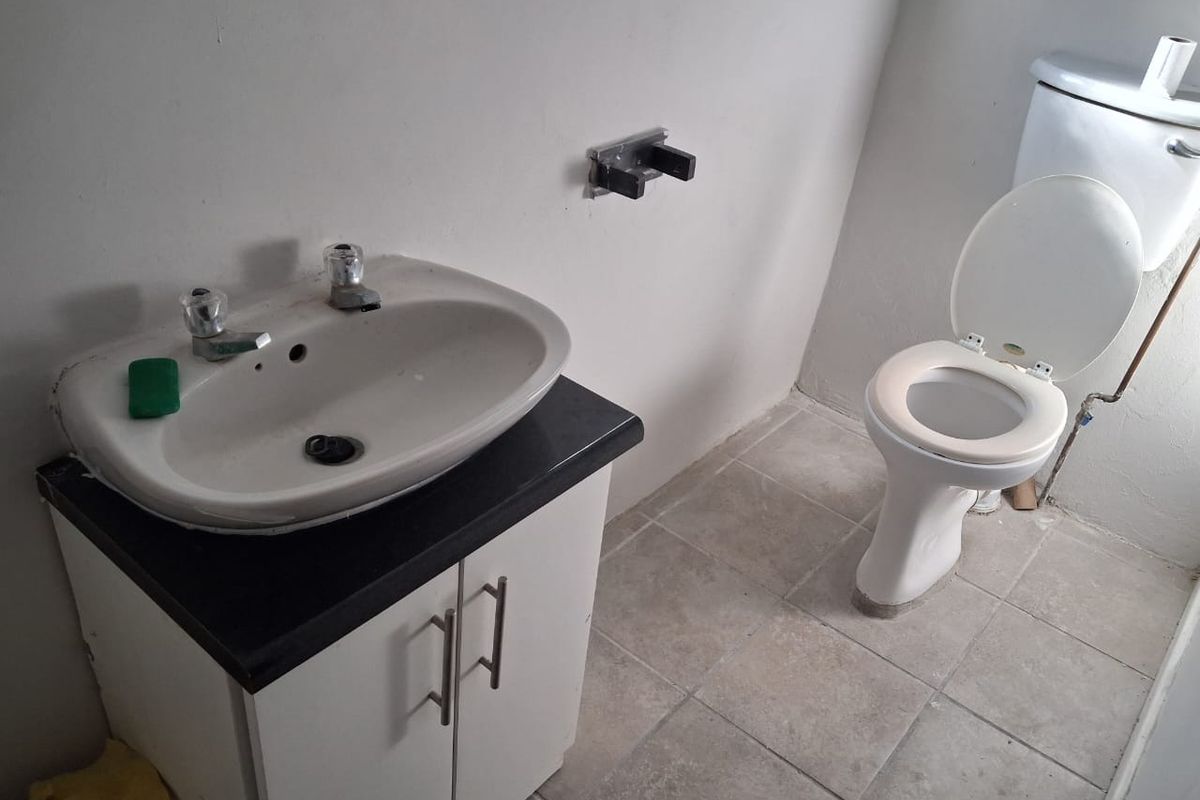 A functional office bathroom featuring a vanity cabinet with a ceramic basin and a standard toilet, finished with tiled flooring.