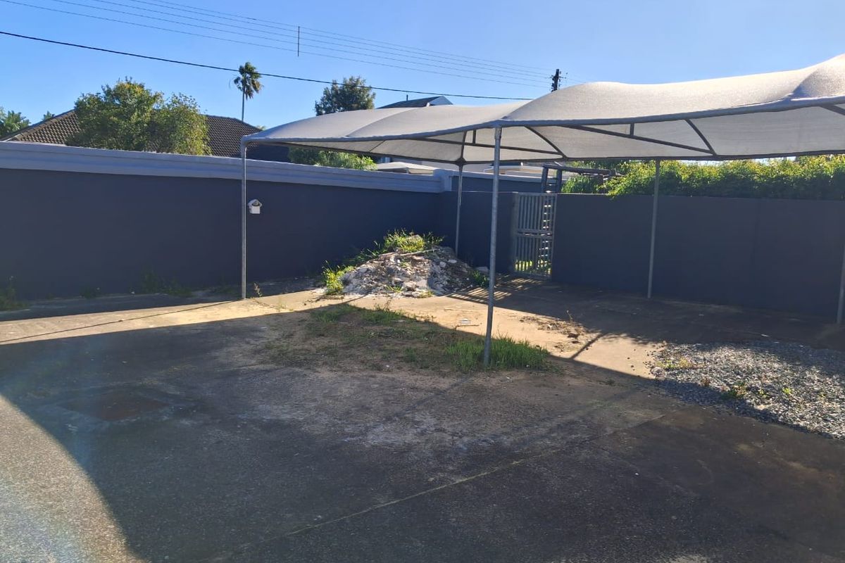 Outdoor paved area featuring a shade cloth carport structure and enclosed by a perimeter wall with a metal gate.