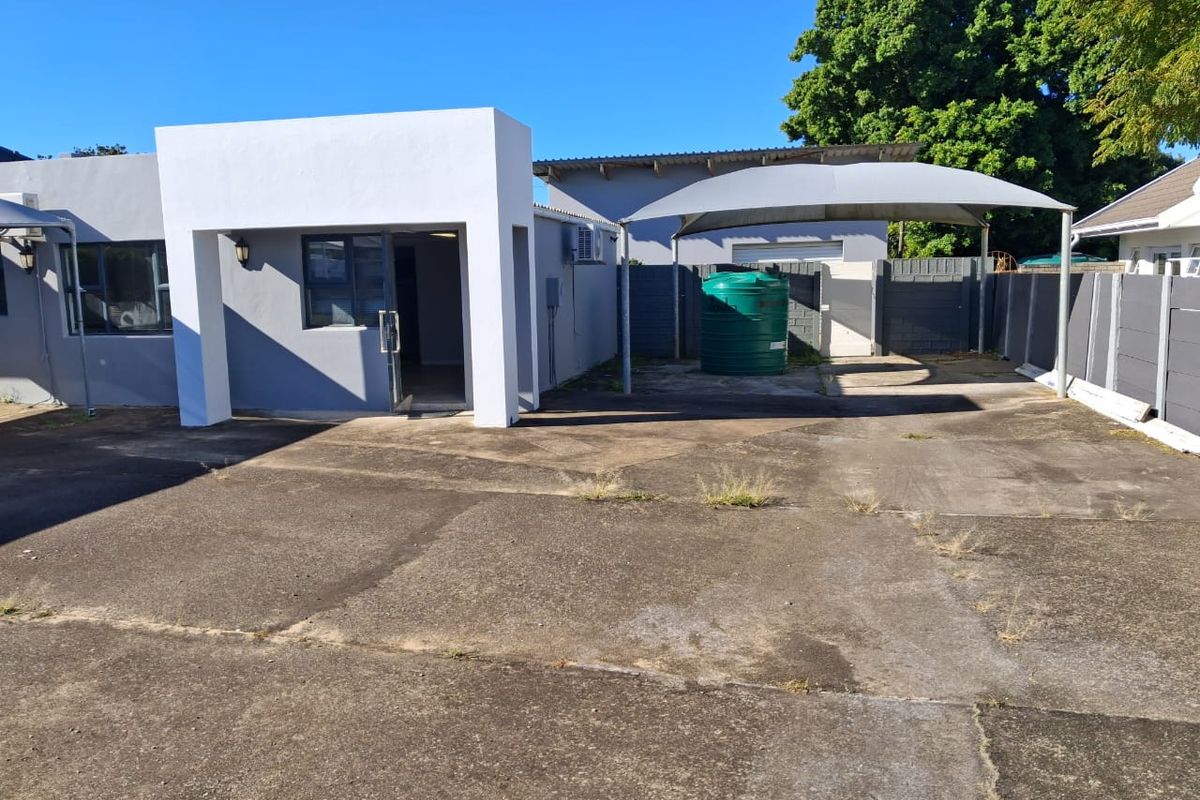 Exterior view of the office property featuring a paved driveway, shade cloth carport, and a water storage tank.