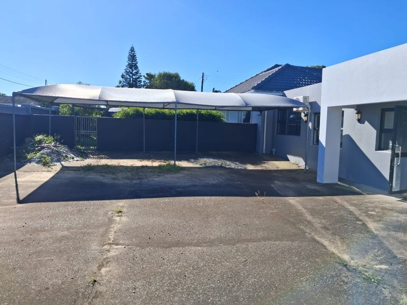 Rear exterior area featuring a concrete driveway, shade cloth carport structure, and perimeter walling.
