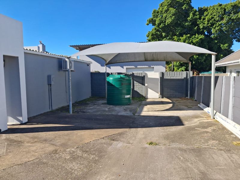 Rear exterior area featuring a concrete paved surface, a shade sail structure, and a water storage tank against a boundary wall.