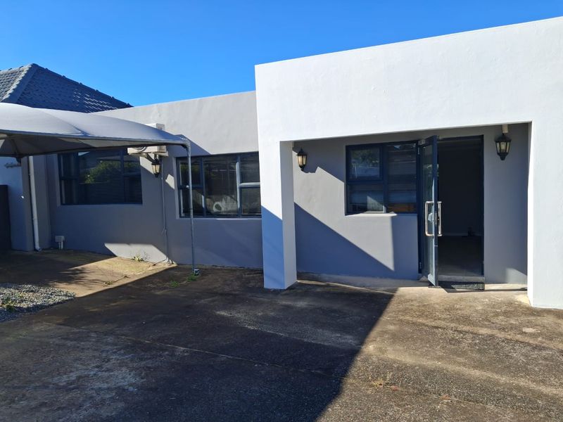 Rear exterior view of the office building featuring concrete paving, a shade sail structure, and aluminium window frames.