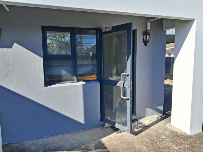 A modern office entrance featuring a grey exterior facade, an aluminium framed glass door, and a matching window with an exterior wall light.