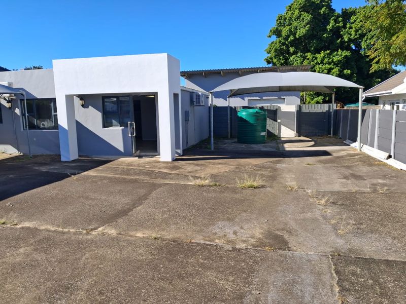 Exterior view of the office property featuring a paved driveway, shade cloth carport, and a water storage tank.