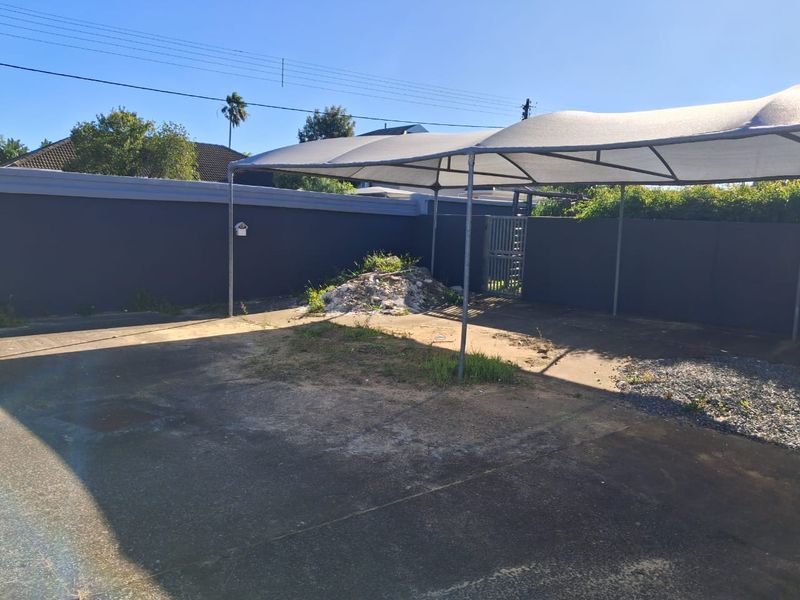Outdoor paved area featuring a shade cloth carport structure and enclosed by a perimeter wall with a metal gate.