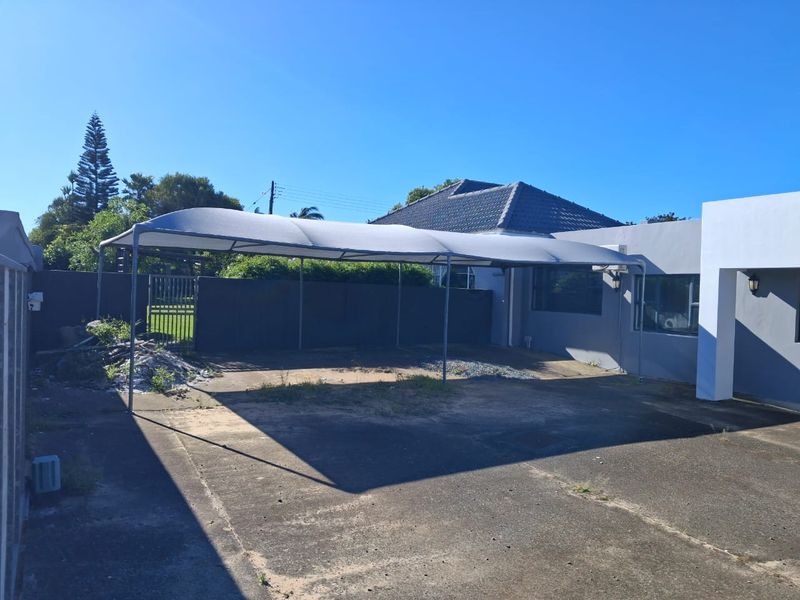 Rear exterior view of the office property featuring a large shade cloth carport, concrete driveway, and perimeter boundary wall.