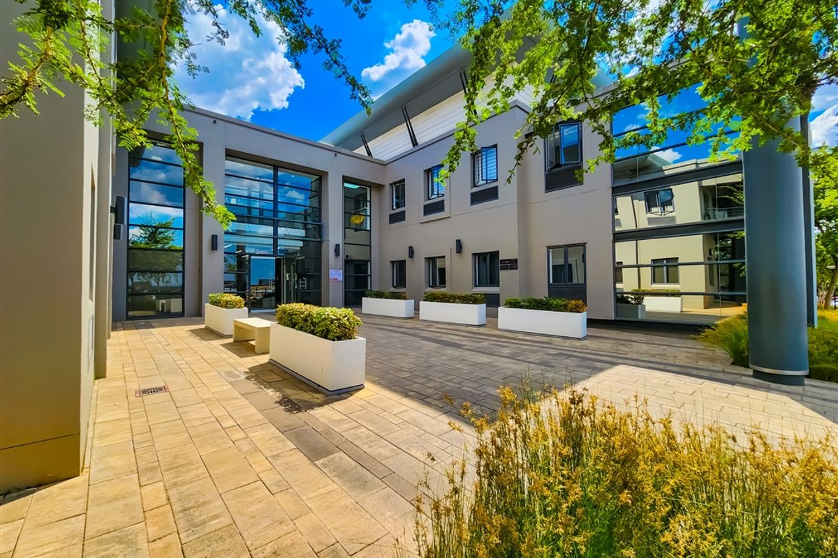 A modern office building exterior featuring a paved courtyard, large glass curtain walls, and contemporary architectural design.
