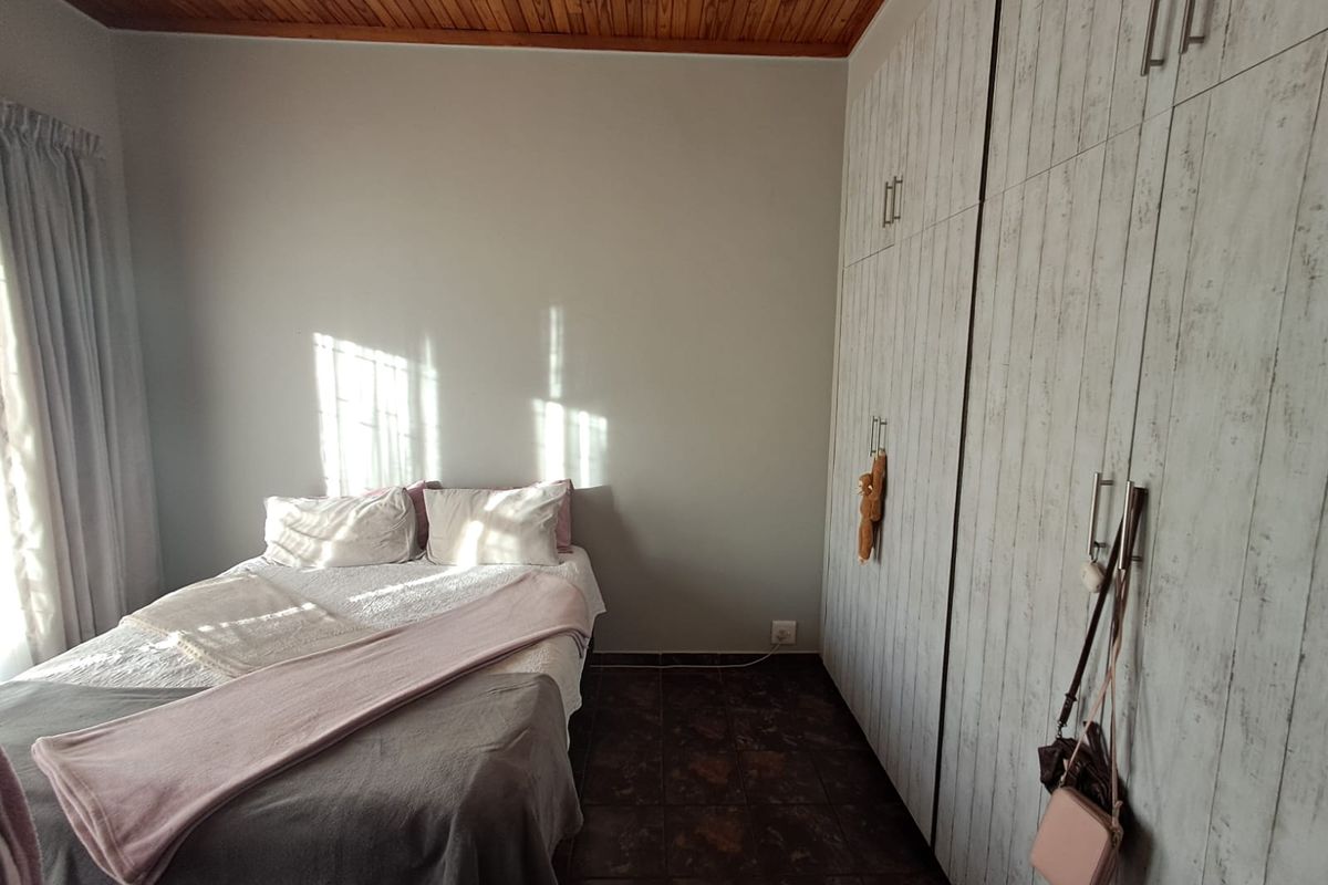 A bedroom featuring built-in cupboards, a timber-clad ceiling, and tiled flooring, offering a functional space with natural light.