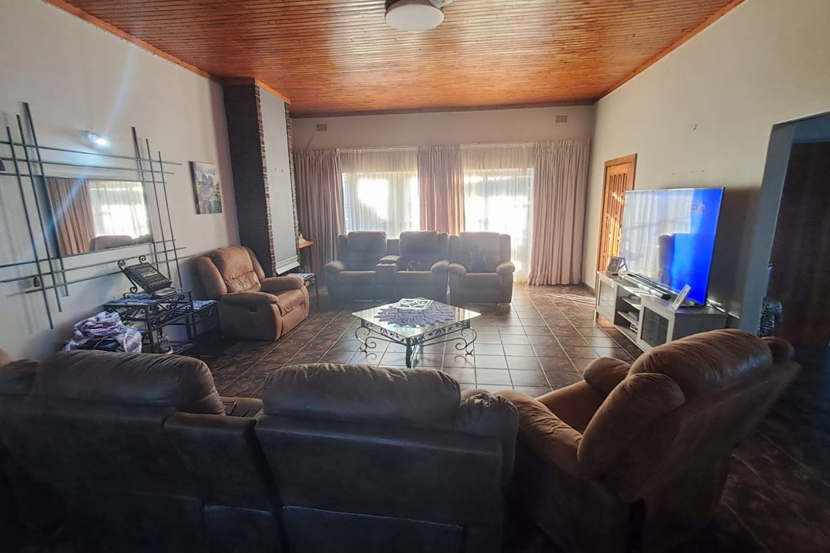 Spacious living room featuring a warm timber tongue and groove ceiling, tiled flooring, and a brick fireplace surround.