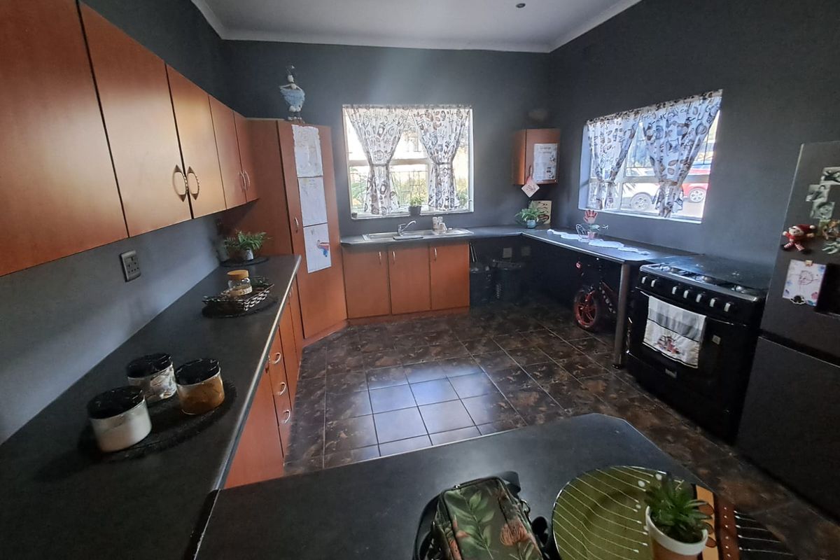 A functional kitchen featuring dark grey walls, wood-tone cabinetry, dark countertops, and tiled flooring, providing a practical workspace with ample storage.