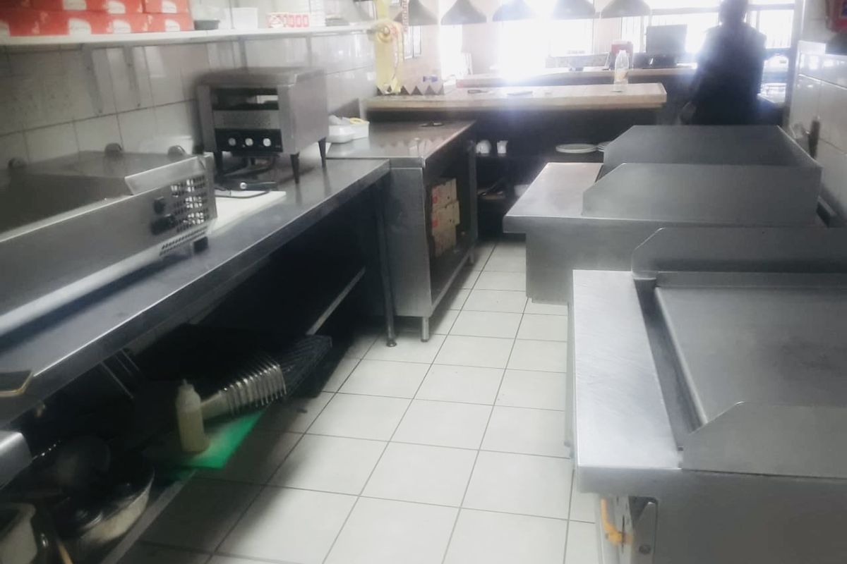 A commercial kitchen space featuring stainless steel work surfaces, tiled flooring, and professional-grade cooking equipment.
