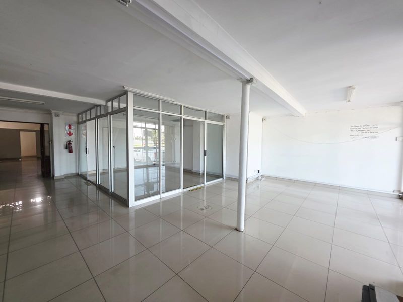 Open-plan office space featuring ceramic tiled flooring, a central support column, and glass-partitioned private office areas.