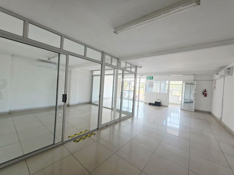 A bright, vacant office space featuring modern aluminum-framed glass partitions, tiled flooring, and integrated air conditioning units, suitable for professional business use.