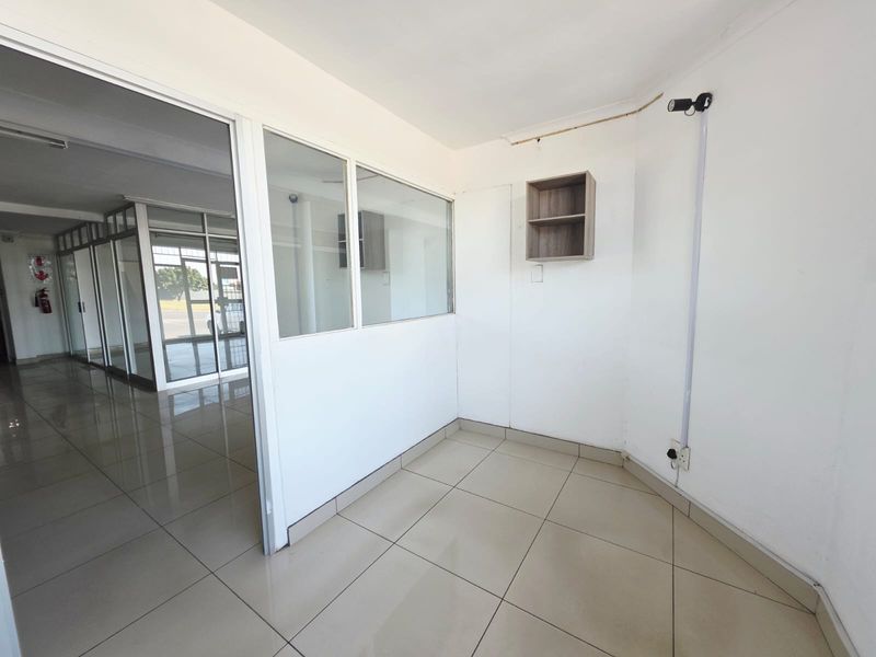 A vacant office space featuring tiled flooring, a glass partition wall, and a built-in wall shelf, suitable for a professional workspace.