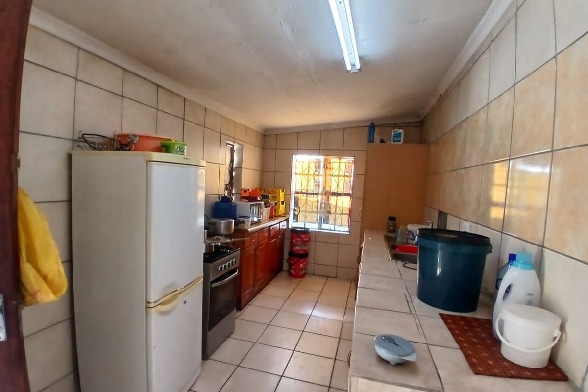 A functional kitchen featuring tiled walls and floors, built-in wooden cabinetry, a stainless steel stove, and a single basin sink.
