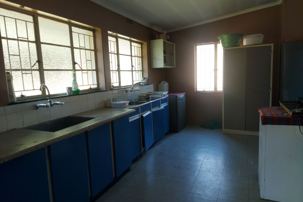 A functional kitchen space featuring built-in blue cabinetry, a stainless steel sink, tiled splashbacks, and large windows with security bars.