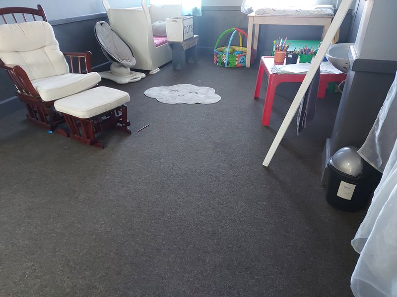 A bedroom space featuring dark carpet flooring and neutral wall finishes, currently utilized as a play area.