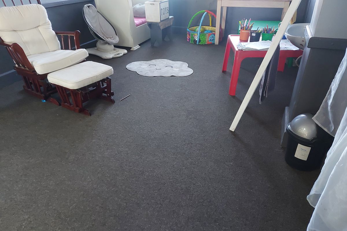 A bedroom space featuring dark carpet flooring and neutral wall finishes, currently utilized as a play area.