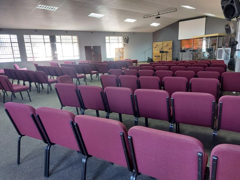 A large commercial assembly hall or clubhouse space featuring carpeted flooring, recessed lighting, and a projector screen, suitable for meetings or events.
