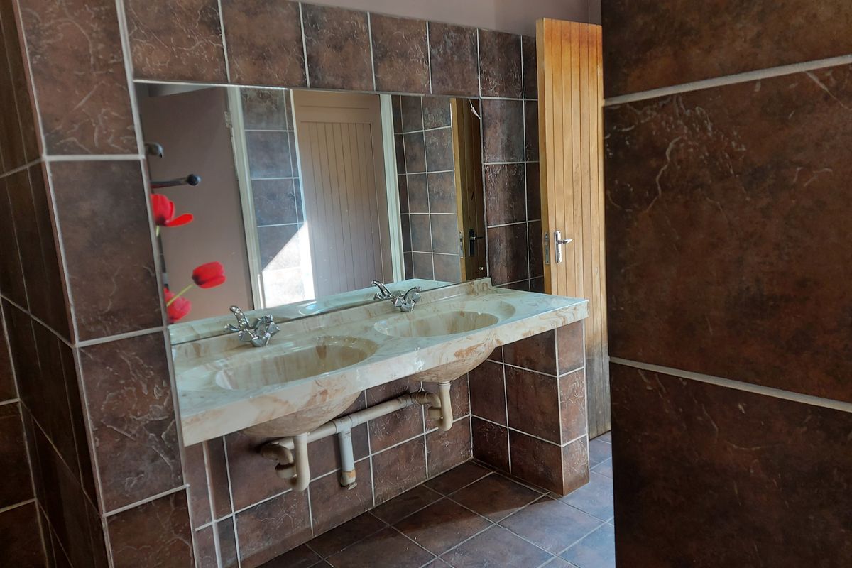 A bathroom featuring a double vanity with a marble-look countertop, large wall-mounted mirror, and full-height brown tiling.