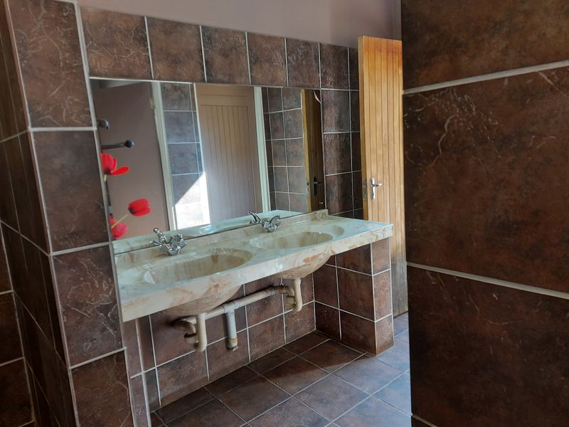 A bathroom featuring a double vanity with a marble-look countertop, large wall-mounted mirror, and full-height brown tiling.